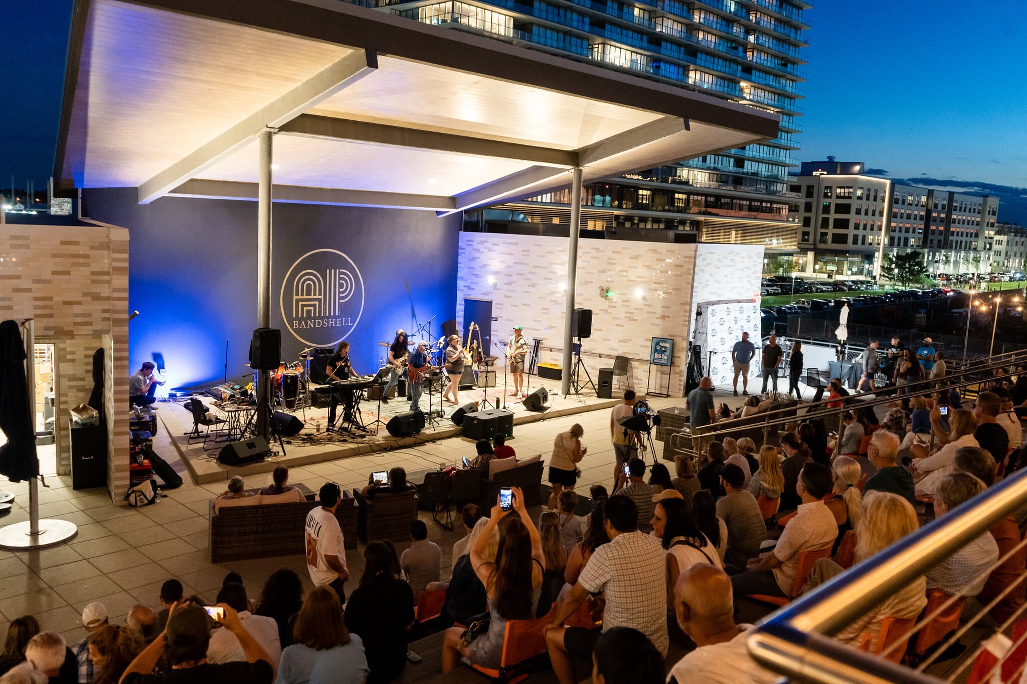 A band performing at the AP Bandshell at night to a packed crowd